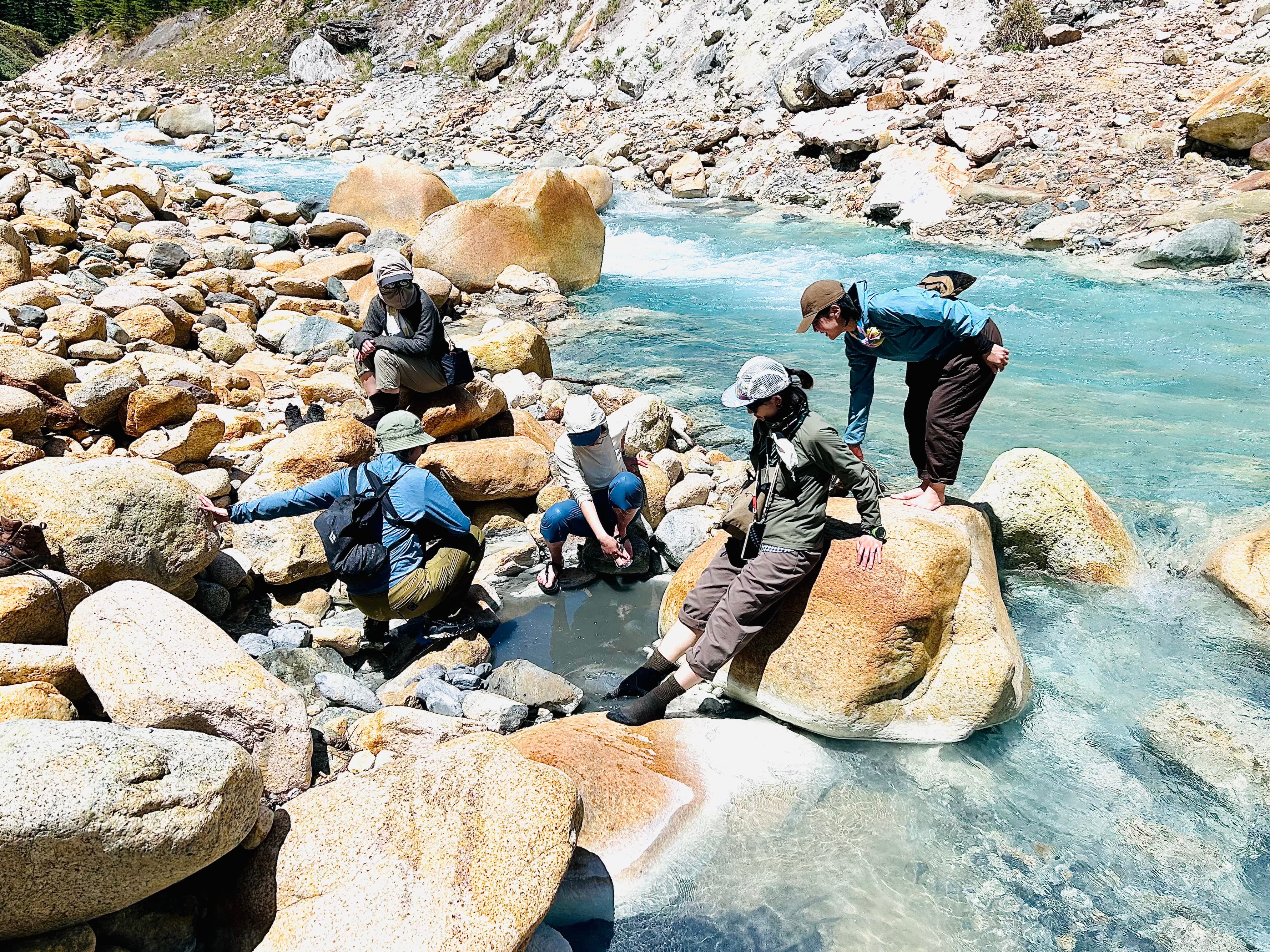 噴湯丘と野湯で岩場に座る登山者たち